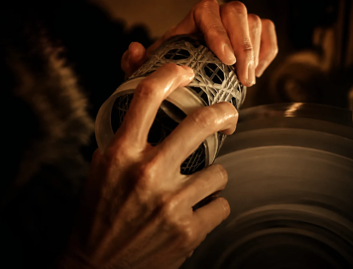Hands working a cut-glass tumbler against a grinding wheel